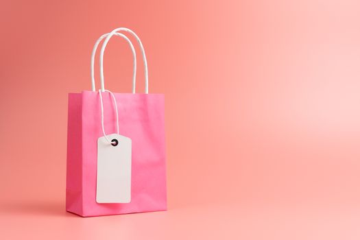 One pink shopping or gift bag with blank label tag isolated on pink background