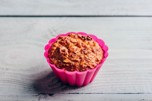 Cooked oatmeal muffin in a pink silicone bakeware over light wooden background.