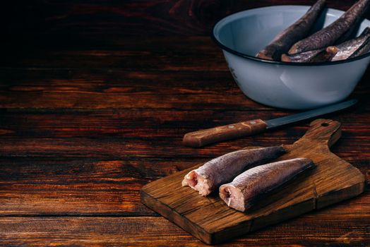 Hake carcasses on cutting board with knife and bowl over wooden surface