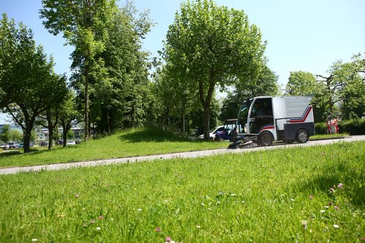 Street cleaning in Switzerland with big cleaning truck with green trees and grass