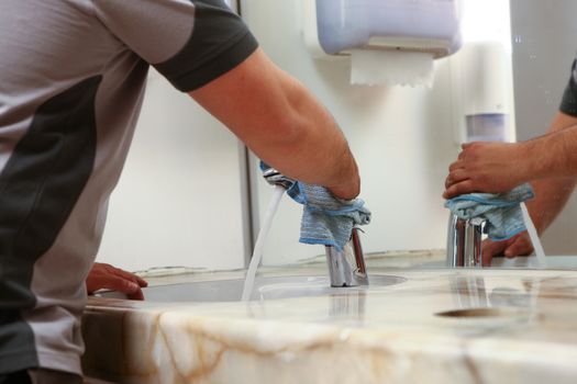 cleaner with rags cleaning a bath room sink, hands and cleaning rag