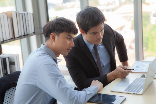 Two young businessmen are discussing business performance data via notebook computers nearing the end of work hours.