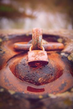 Close up of a rusty padlock locked around an aged rusty iron ring in a puddle of water. Time and aging concept.