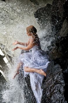 Young blonde woman in a white wedding dress near the waterfall