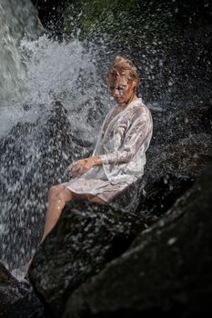 Young blonde woman in a white shirt swimming in a waterfall