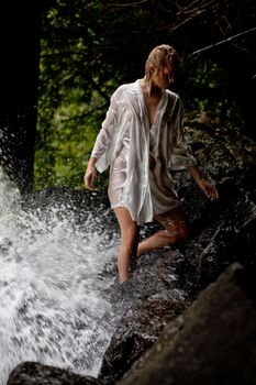 Young blonde woman in a white shirt swimming in a waterfall