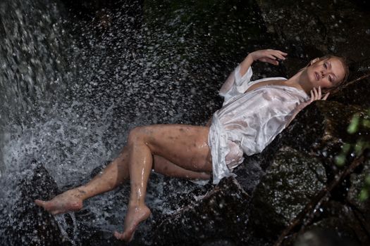 Young blonde woman in a white shirt swimming in a waterfall