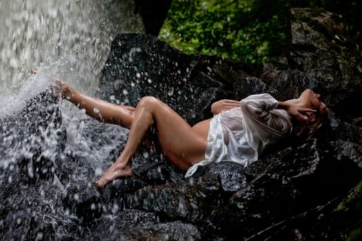 Young blonde woman in a white shirt swimming in a waterfall