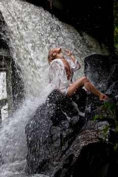 Young blonde woman in a white shirt swimming in a waterfall