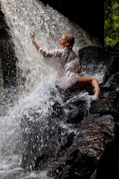 Young blonde woman in a white shirt swimming in a waterfall