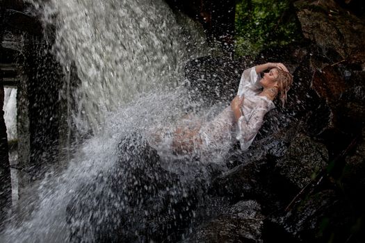 Young blonde woman in a white shirt swimming in a waterfall