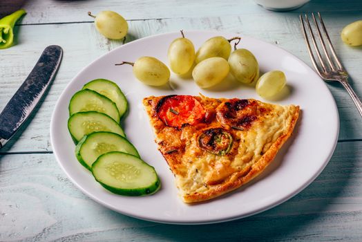 Breakfast frittata with sliced cucumber, and green grapes on white plate over wooden background.