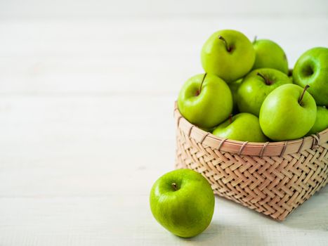 Apples harvest concept. Braided Bamboo Basket with green apples on white wooden background with copy space for text or design.