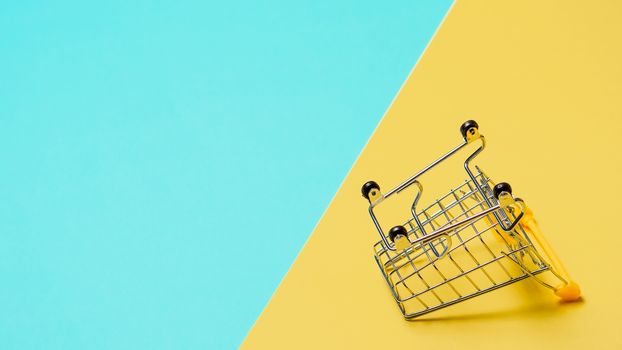 Empty inverted shopping cart on blue and yellow background. Inverted toy trolley on bright colorful background, copy space for text or design.