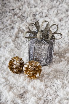 Silver wrap present and gold plated pine cone in the snow