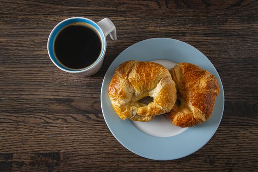 top view of a black coffee and croissant against a dark wood background