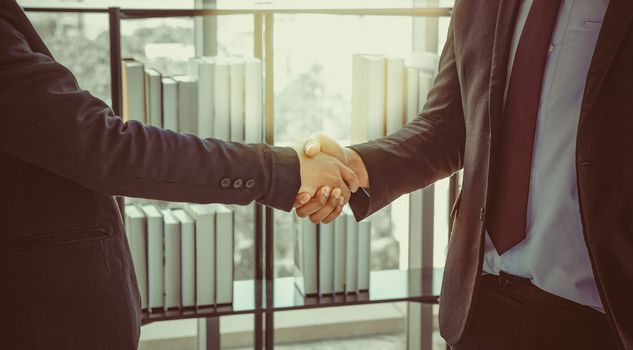 Two young businessmen shaking hands to celebrate in the office success with a turnover that exceeds corporate goals. Color in vintage look.