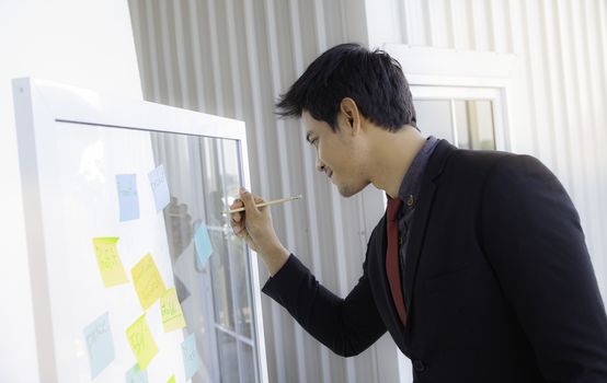 A young businessman smiled happily, recording his creativity on a sticky note affixed to a glass in a modern office.