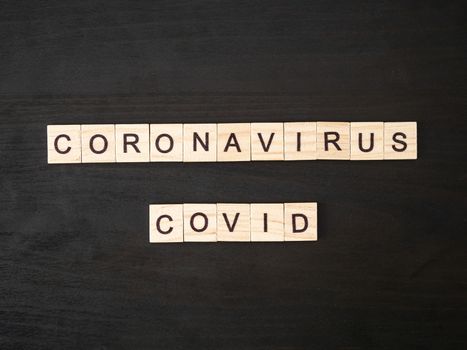 Coronavirus COVID words made of wood block. Coronavirus COVID text on dramatic atmosphere black wooden table. Coronavirus concept top view.