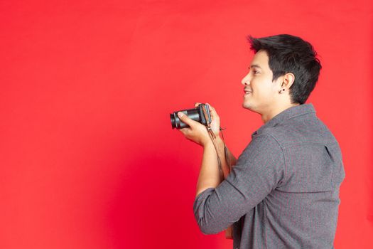 Young Asian hipster man searching for an interesting subject on the studio on a red background.Travel Lifestyle concept