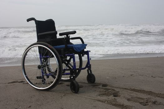 wheelchair left alone on a beach by the sea in winter without sick or other people