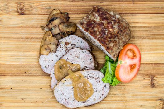 Meatloaf cut into slices with mushrooms, tomato and salad top view on an isolated wooden background.