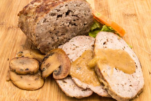 Meatloaf cut into slices with mushrooms, tomato and salad on an isolated wooden background.