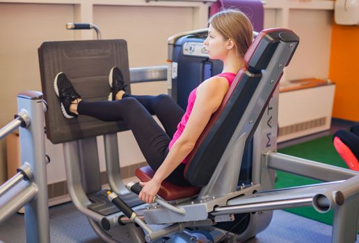 Woman doing fitness training on leg extension push machine with weights