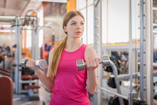 Active woman lifting dumbbells in the gym