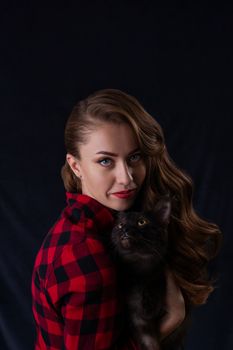 Fashion photo of pretty girl with black maine coon cat on hands. Maine coon cat with beautiful woman on gray background.