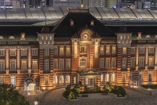 Night view of Marunouchi side of Tokyo railway station in the Chiyoda City, Tokyo, Japan.  The station is divided into Marunouchi and Yaesu sides in its directional signage. The station first called Central Station was built in 1914 directly in front of the Imperial Palace gardens. The three-story station building was designed by architect Tatsuno Kingo who also designed Manseibashi Station and the nearby Bank of Japan building. Much of the station was destroyed in B-29 firebombing on May 25, 1945. The bombing shattered the impressive rooftop domes. The station was quickly rebuilt within the year, but simple angular roofs were built in place of the domes, and the restored building was only two stories tall instead of three. 