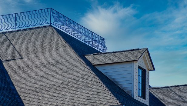 A dormer on a grey shingled roof with widow's walk