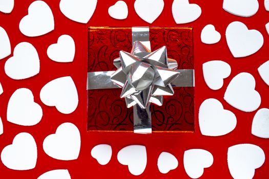 A present on a red background with white hearts. For Valentine’s Day