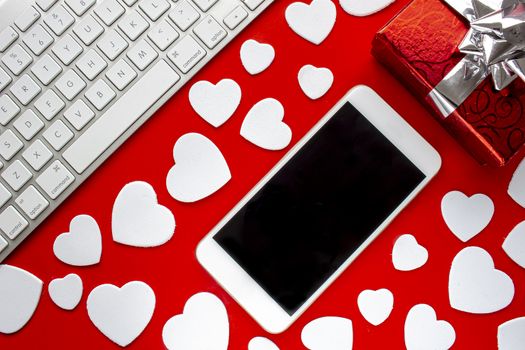 A smart phone with a keyboard a present and hearts on a red background with hearts
