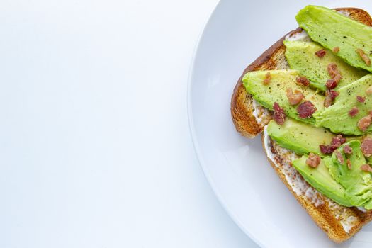 Close up of an avocado toast with bacon bites on a white plate on the right