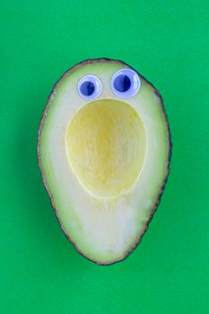 An avocado cut in half on a green background with Black Wiggle Googly Eyeballs