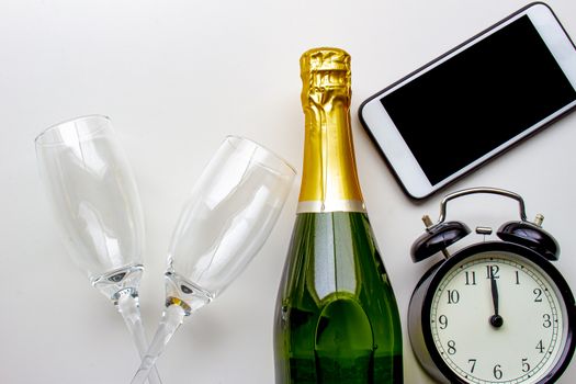 Unopened champagne bottle with empty cups, clocks and smart phone on a white background