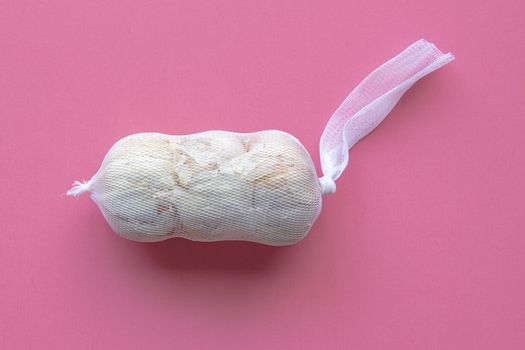 A bag of white heads of garlic on a pink background