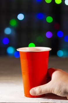 Hand holding a one use cup with lights on the background