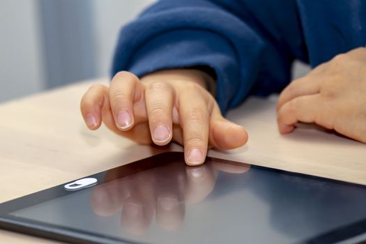 Close up front view of a little boy's hand using and black tablet with a privacy camera cover, during the day time