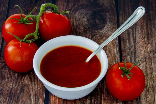 Fresh tomatoes sauce on a wood table and a plate with a spoon and  tomato berries on the side.