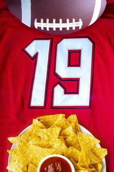 An American football with organic nacho chips and mild salsa on a white red football jersey with the 19 number