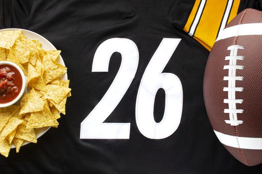 An American football with organic nacho chips and mild salsa on a white black football jersey with the 26 number on horizontal view