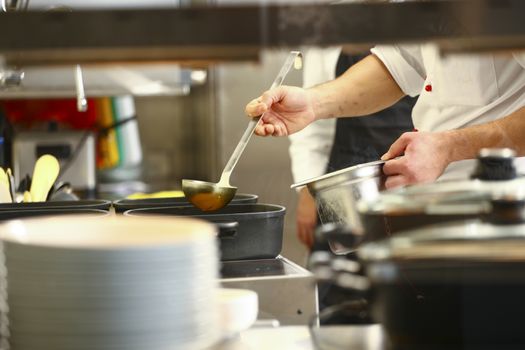 professional cook in kitchen preparing food for customers showing hands and a cook grabbing some yellow sauces