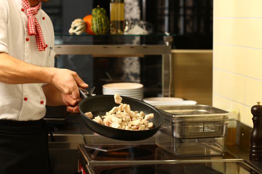 professional cook in kitchen preparing food for customers showing hands and and a pan with pieces of chicken