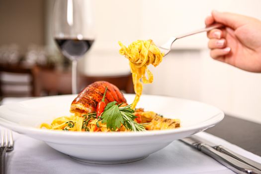 Close up of a plate pasta with shrimp. With a fork taking some pasta and a glass wine in background