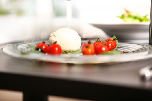 mozzarella and tomatoes served on a plate with balsamic with a salad out of focus