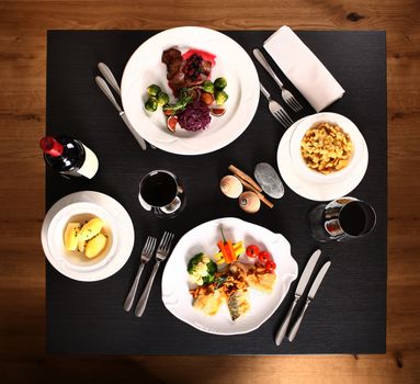 Black table with four white plates and wine on a wooden restaurant floor