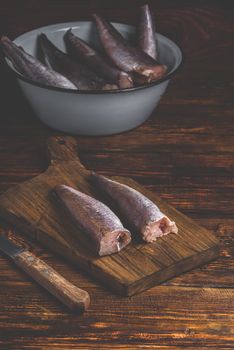 Hake carcasses on cutting board with knife and bowl over wooden surface