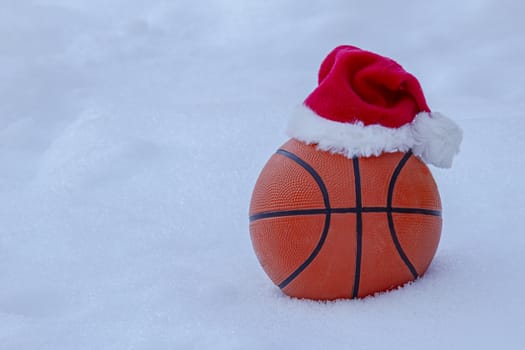 Basket ball wearing a santa hat on snow during winter